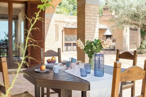 Une table de jardin, dressée pour un repas en plein air, avec des assiettes, des tasses et un vase rempli de fleurs.