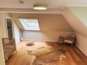 A room with a sloped ceiling, a skylight, a wooden floor, a small round table, a chair, and a large fur rug. - Cosy apartment for 5 people with TV and patio (Ringstedt)
