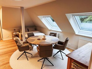 Ein modernes Schlafzimmer im Loft-Stil mit schrägverdeckter Decke, einem runden Holzesstisch und Blick durch Dachfenster.
