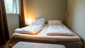 A double bed with a bench in front, a bedside table, and a window with curtains. - North Nest Signature Apartment (Tromsø)
