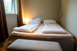 A double bed with a bench in front, a bedside table, and a window with curtains. - North Nest Signature Apartment (Tromsø)