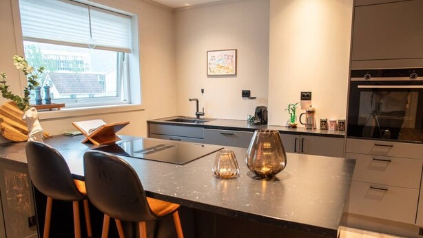 A modern kitchen with a central island, bar stools, a window with blinds, and a coffee machine. - North Nest Signature Apartment (Tromsø)