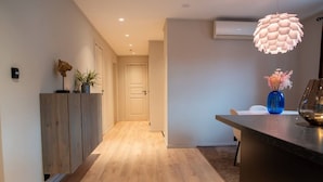 A modern interior with a wooden floor, a kitchen area with a blue vase, and a hallway leading to a door. - North Nest Signature Apartment (Tromsø)