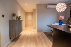 A modern interior with a wooden floor, a kitchen area with a blue vase, and a hallway leading to a door. - North Nest Signature Apartment (Tromsø)