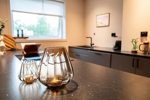 A kitchen counter with two glass candle holders, a window with blinds, and a sink. - North Nest Signature Apartment (Tromsø)