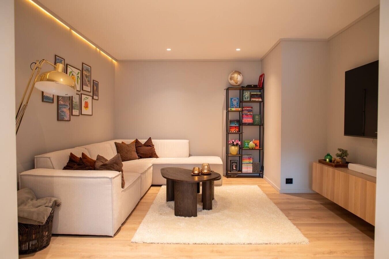 Ein modernes Wohnzimmer mit einem weißen Sofa, einem Couchtisch, einem Bücherregal und einem Flachbildfernseher.