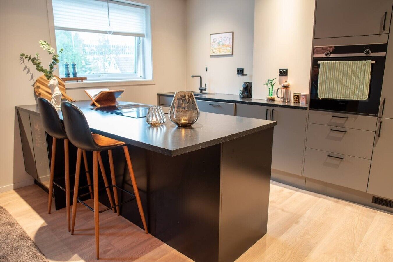 A modern kitchen with a central island, bar stools, a window with a view, and a built-in oven.