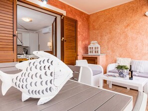 Ein Zimmer mit Esstisch, weißen Stühlen, einer Couch, einer dekorativen Fischskulptur und einer kleinen weißen Laterne auf einem Regal.