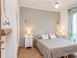 Ein Schlafzimmer mit einem Bett, zwei Nachttischen, einem Deckenventilator und einem Fenster mit Vorhängen.