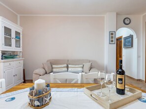 Ett mysigt vardagsrum med en soffa, ett matbord med vinglas och en vinflaska samt ett skåp med glasvaror.