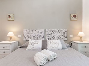 Un lit bien fait, avec deux oreillers, une table de chevet avec une lampe et des œuvres d’art décoratives accrochées au mur.