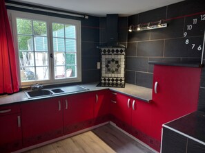 Une cuisine avec des meubles de couleur rouge, un pare-feu noir, une fenêtre donnant sur un beau paysage et une horloge au mur.