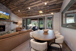 A modern interior with a stone fireplace, a wooden ceiling, and a dining area with a large table and chairs. - Brand New Townhome Across from Purg - Hot Tub/Arcade Game/Views/EV Charger/AC (Durango)