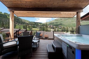 Eine Holzterrasse mit Sitzgelegenheiten und einem Whirlpool mit Blick auf eine gebirgige Landschaft.