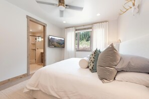 Ein Schlafzimmer mit einem Bett, einem Fernseher, einem Fenster mit Vorhängen und einem Deckenventilator.