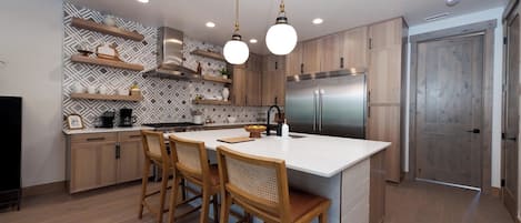 Eine moderne Küche mit einer zentralen Kochinsel, Holzbarhocker und eingebauten Holzausziehtischen.