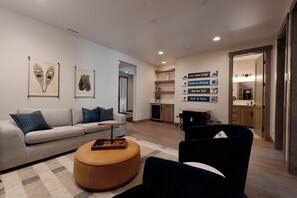 A modern living room with a sofa, ottoman, and a dark armchair. There are wall-mounted signs indicating directions to nearby locations. - Brand New Townhome Across from Purg - Hot Tub/Arcade Game/Views/EV Charger/AC (Durango)