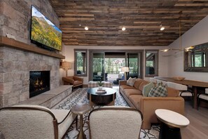 A modern living room with a stone fireplace, leather sofas, a coffee table, and a television mounted on the wall. - Brand New Townhome Across from Purg - Hot Tub/Arcade Game/Views/EV Charger/AC (Durango)