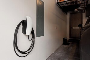 Un couloir avec une borne de recharge pour véhicules Tesla, une porte et une poubelle.