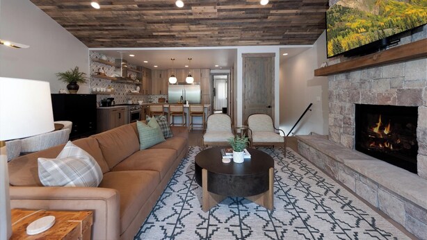 A modern living room with a stone fireplace, a sofa, a coffee table, and a kitchen in the background. - Brand New Townhome Across from Purg - Hot Tub/Arcade Game/Views/EV Charger (Durango)
