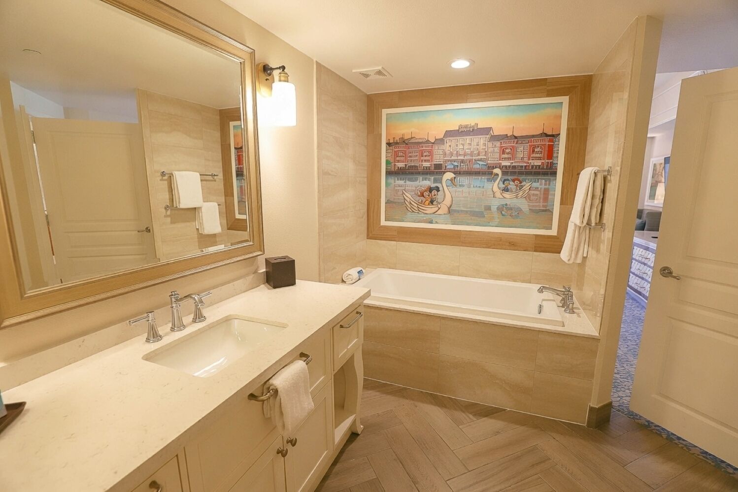 A bathroom with a double sink, a bathtub, a large mirror, and a painting of swans on a river.