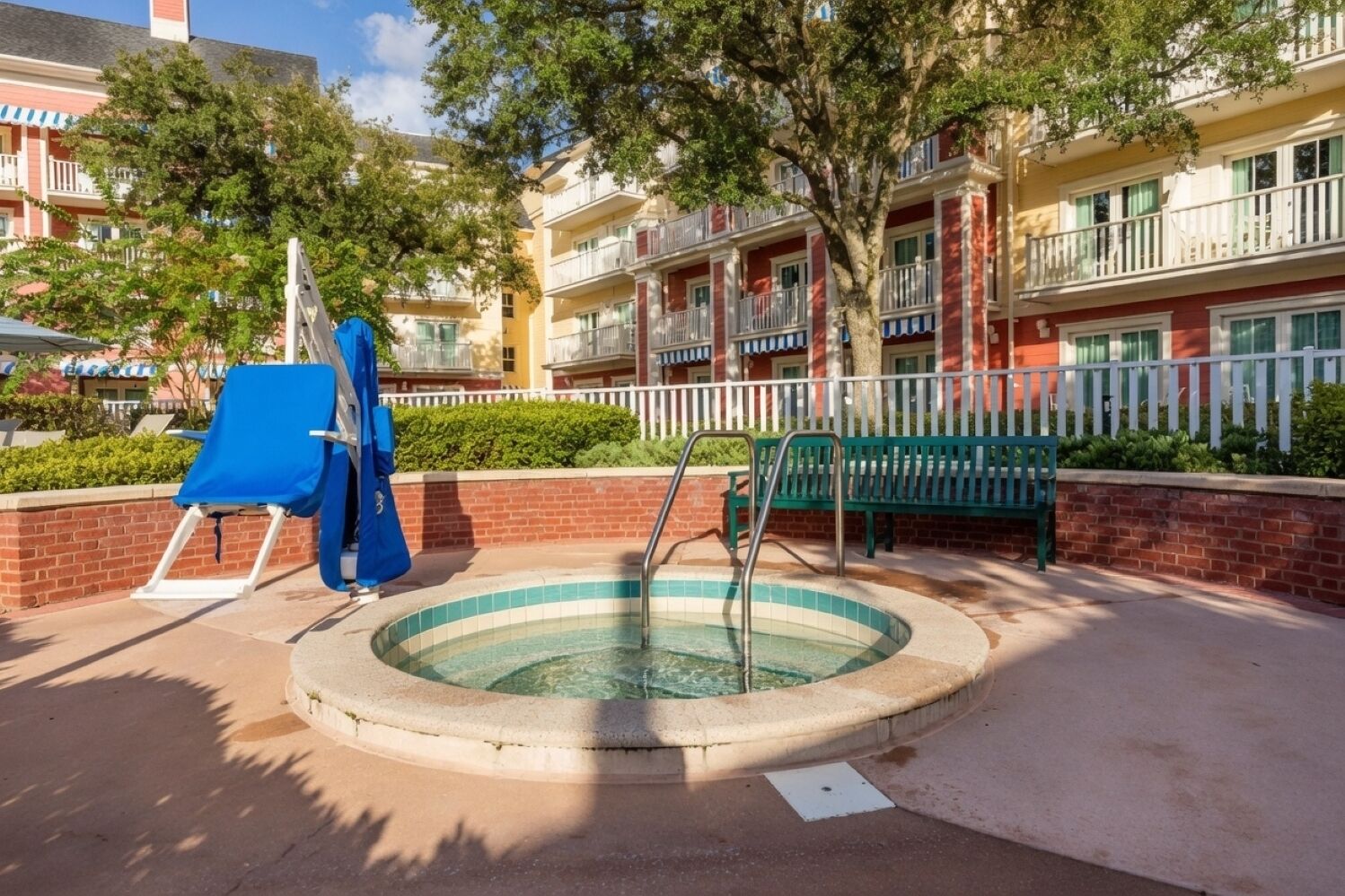 A pool area with a circular hot tub, a blue slide, and a green bench.