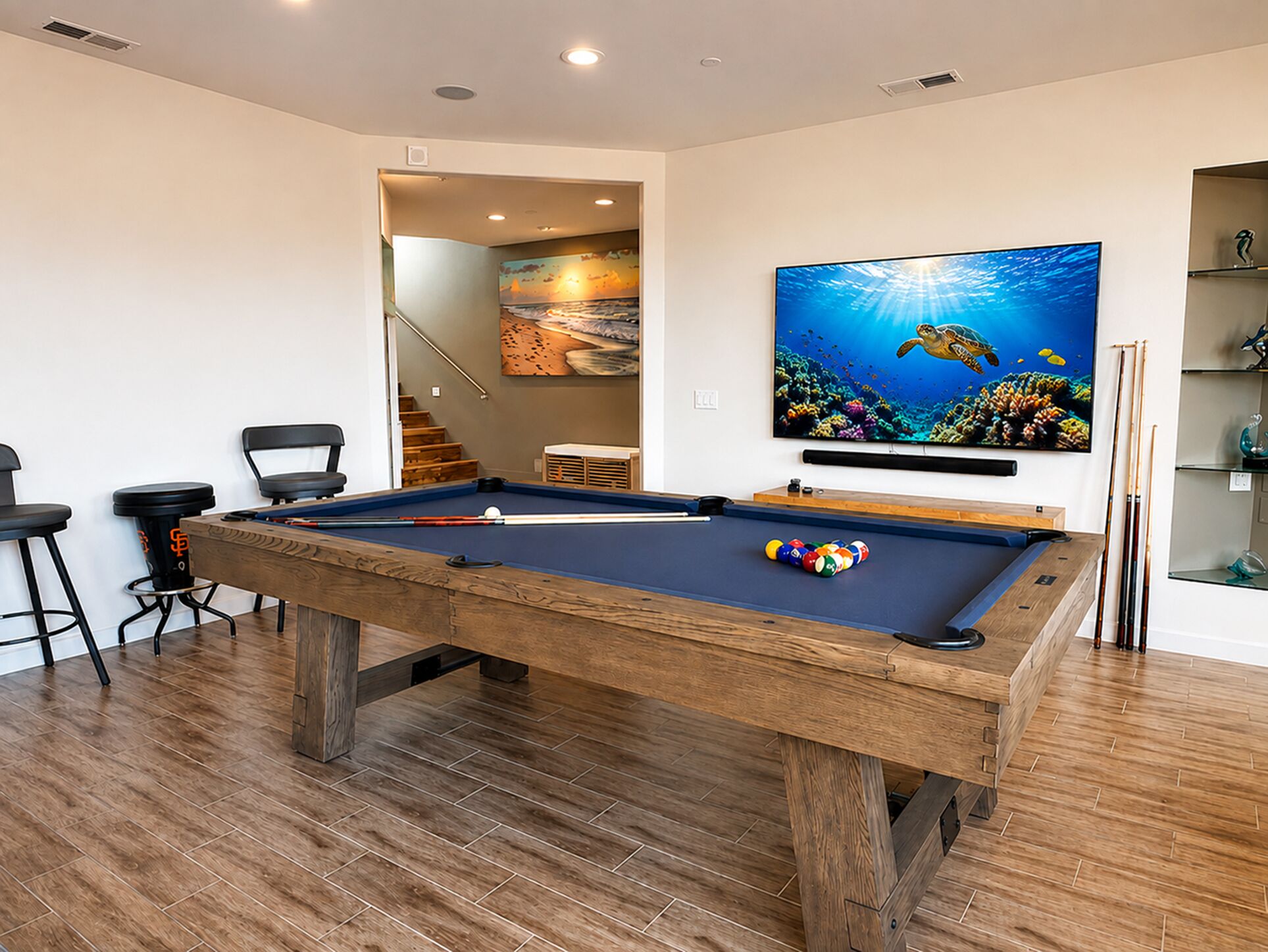 A pool table with a wooden frame, a pool cue, and balls, a bar stool, and a television displaying an underwater scene.
