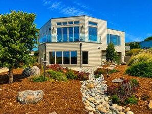A modern two-story house with a landscaped garden featuring rocks, mulch, and various plants. - Bodega Bay~5BR~Hot Tub~Game Room~Golf~Near Doran Beach~Coastal View~Sleeps 12 (Bodega Bay)