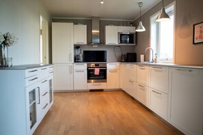 A modern kitchen with white cabinetry, a built-in oven, microwave, and a coffee maker. - Spacious Aurora Family Home (Tromsø)