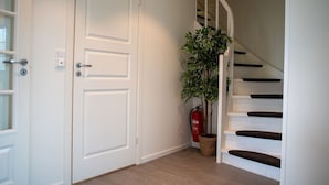 A staircase with a white handrail and wooden steps, a white door with a keyhole, and a potted plant beside a fire extinguisher. - Spacious Aurora Family Home (Tromsø)
