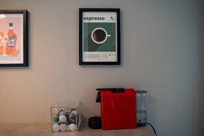 Ein gerahmter Espresso-Werbeaufsteller, eine Kaffeemaschine, ein Wasserspender und eine Kanne mit Tassen auf einer Theke.