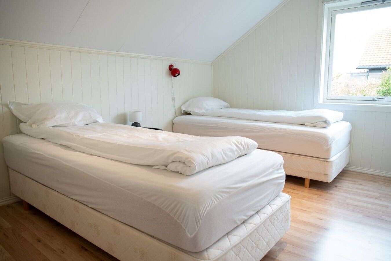 A room with two beds, a window, and a wall-mounted red object.