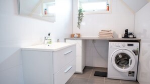 A modern bathroom with a white vanity, a washing machine, and a window with a plant. - Spacious Aurora Family Home (Tromsø)