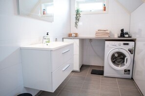 Ein modernes Badezimmer mit einem weißen Waschtisch, einer Waschmaschine und einem Fenster mit Pflanze.