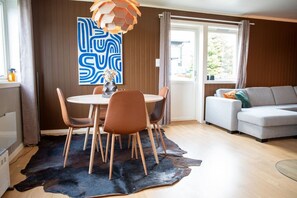 Ein modernes Wohnzimmer mit einem runden Esstisch, Ledersesseln, einem grauen Sofa und einem großen abstrakten Gemälde an der Wand.