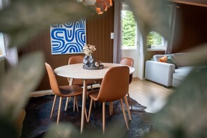 Ein Essbereich mit einem runden Tisch und Stühlen, einer Blumenvase und einem blauen, abstrakten Gemälde an der Wand.