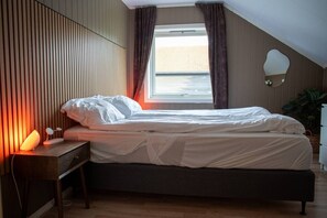 A bedroom with a bed, bedside table, lamp, and a window with curtains. - Spacious Aurora Family Home (Tromsø)