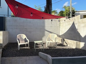 Un patio con dos sillas de plástico y una mesa pequeña, rodeado de grava y paredes de concreto.