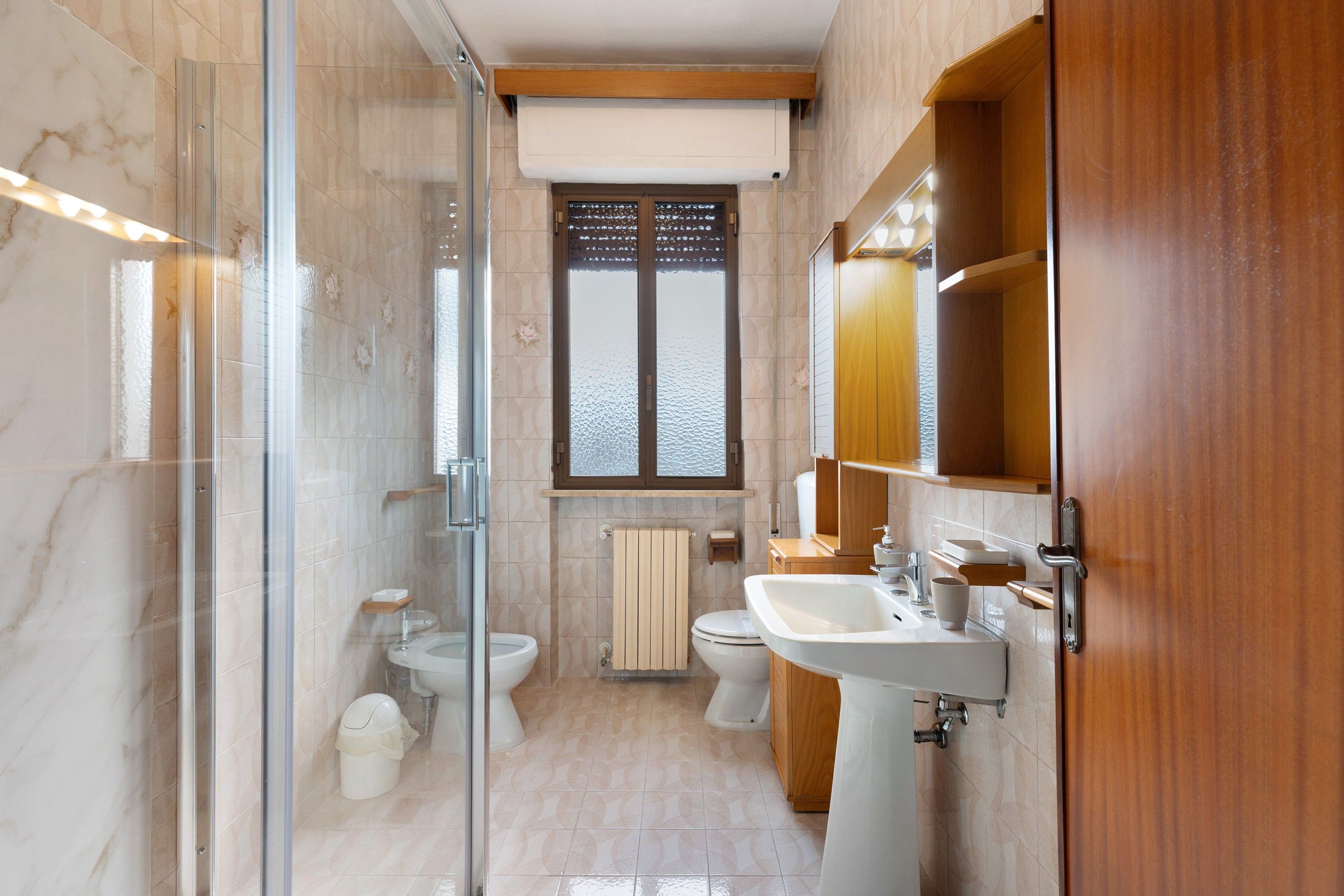 Ein modernes Badezimmer mit Duschkabine aus Glas, Toilette, Bidet und Waschbecken mit Holzschrank.