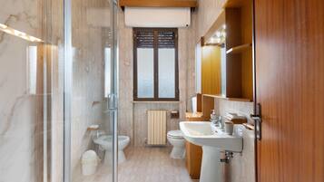 Ein modernes Badezimmer mit Duschkabine aus Glas, Toilette, Bidet und Waschbecken mit Holzschrank.