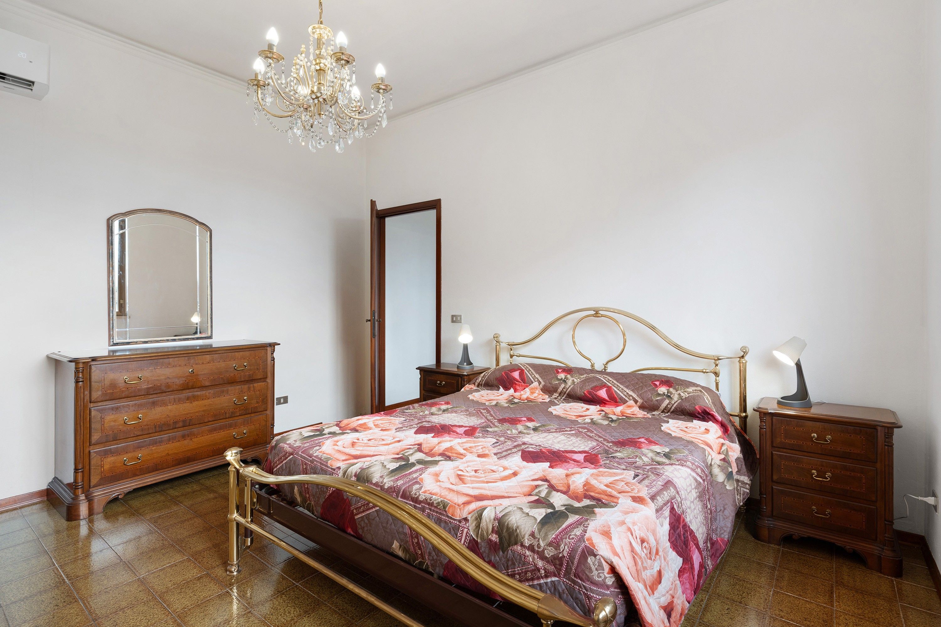 Ein Schlafzimmer mit Bett, Schminktisch, Nachttischen, einer Chandelüster und einem Spiegel.