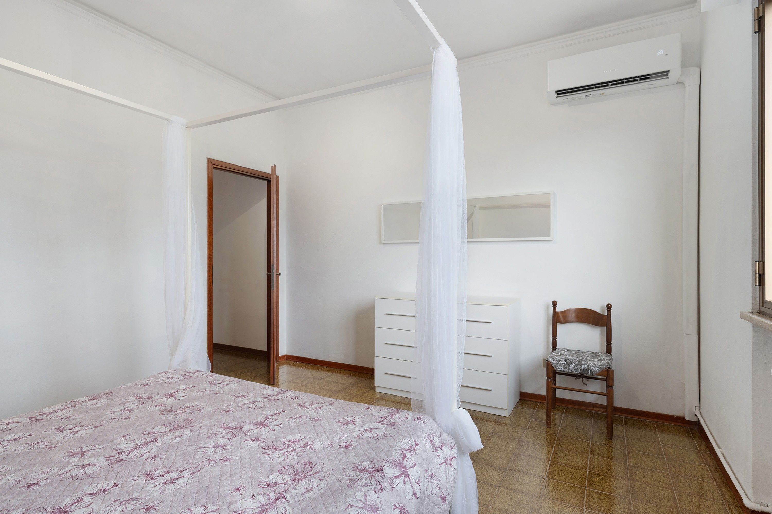 Ein Schlafzimmer mit Bett, Stuhl, Kommode, Klimaanlage und Tür.