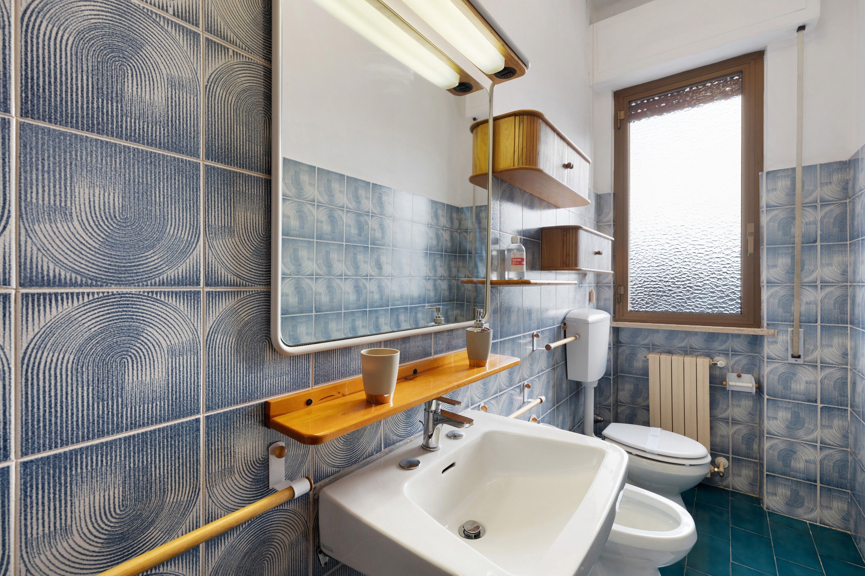 Ein Badezimmer mit Waschbecken, Toilette und Spiegel. Ein Fenster bietet Blick auf das Wasser.