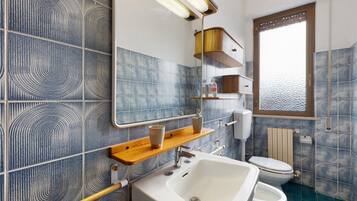 Ein Badezimmer mit Waschbecken, Toilette und Spiegel. Ein Fenster bietet Blick auf das Wasser.