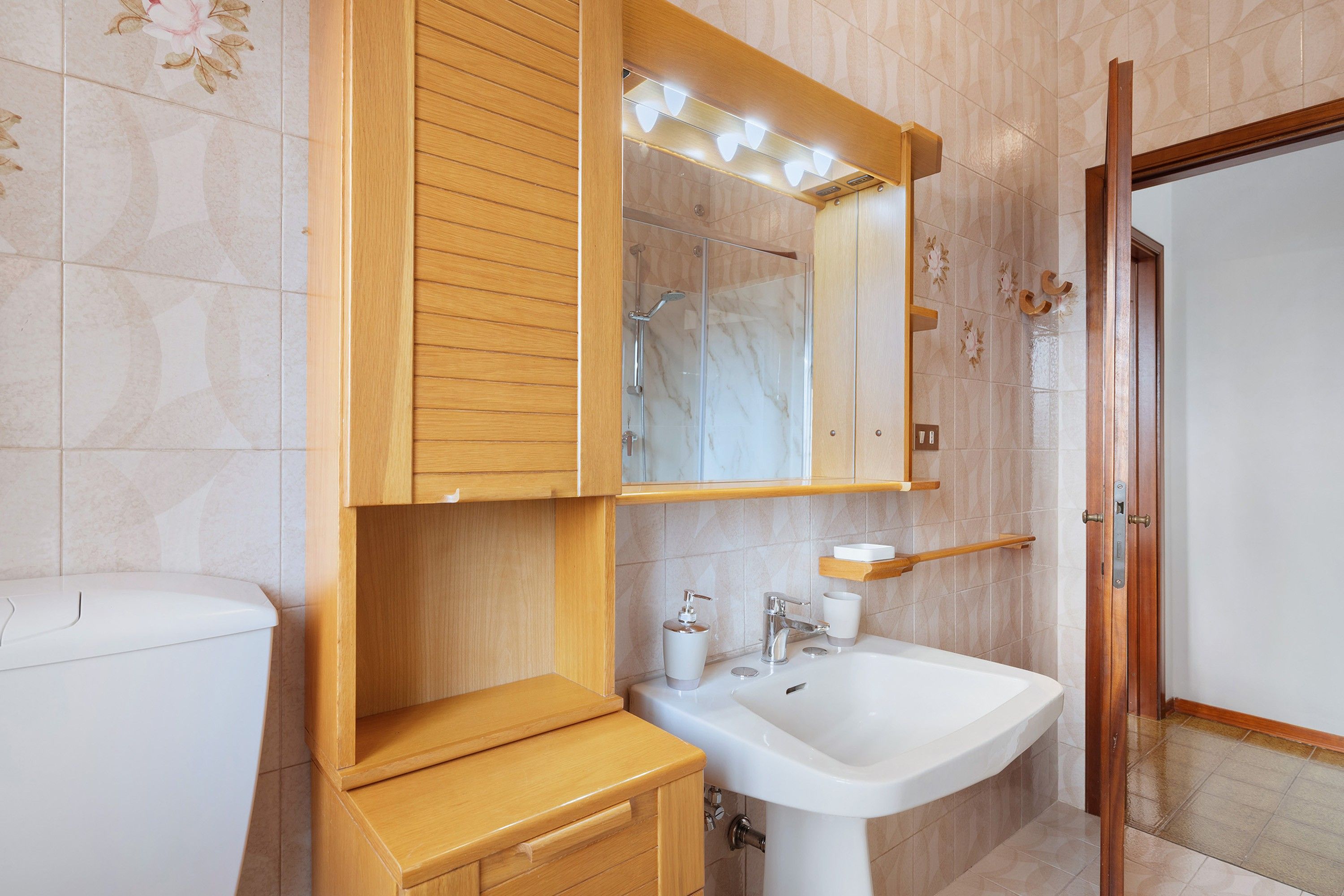 Ein Badezimmer mit einem Holzkosmetikschrank, einem weißen Waschbecken und einem Spiegel darüber.