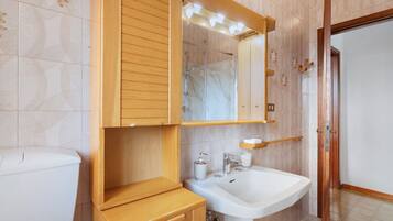 Ein Badezimmer mit einem Holzkosmetikschrank, einem weißen Waschbecken und einem Spiegel darüber.