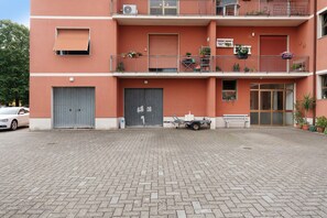 Un edificio de varios pisos con fachada roja, balcones con macetas y un patio empedrado.