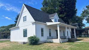 A white two-story house with a porch, a stone foundation, and a large tree in the background. - Spacious 4-bedroom house in Franklin Kentucky (Franklin)