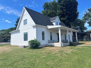 A white two-story house with a porch, a stone foundation, and a large tree in the background. - Spacious 4-bedroom house in Franklin Kentucky (Franklin)