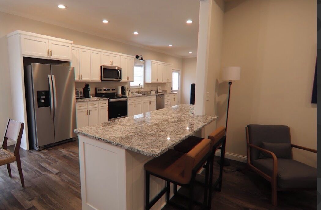 A modern kitchen with white cabinets, stainless steel appliances, a granite countertop, and a bar stool.